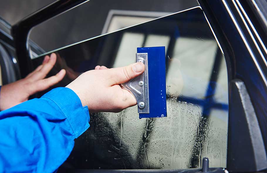 car tinting. Automobile mechanic technician applying foil on window in repair garage workshop